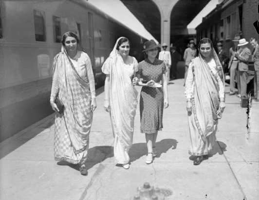 Four Indian women walk through Union Station in Denver, Colorado. Three of the women wear saris and one is dressed in a dress and hat.