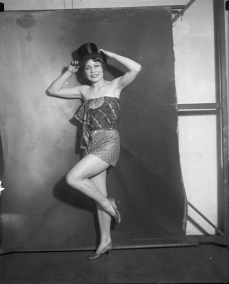 A young woman poses in a costume that includes shorts, high heels, print fabric, and a stovepipe hat.
