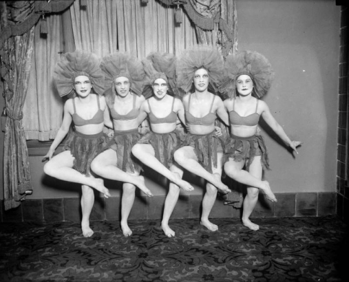 Members of the Georgia Lane Group, from the Georgia Lane School of Dancing, pose in a chorus line in Denver, Colorado; the women wear taffeta headdresses, skirts with fringe, and halter tops. Sarah Francis "Sally" Orr is in the center of the chorus line.