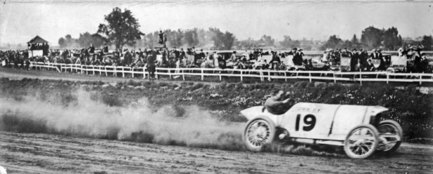 View of a dirt track auto race with car #19, probably at Overland Park in Denver, Colorado. Spectators watch from behind the fence.