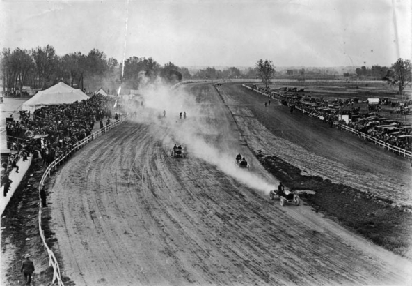 Overlook view of race cars on a dirt track, probably Overland Park in Denver, Colorado. Spectators watch from the sidelines.