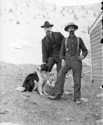 Men pose with a dog; clothing includes hats and suspenders; one man smokes a pipe, probably in Colorado.