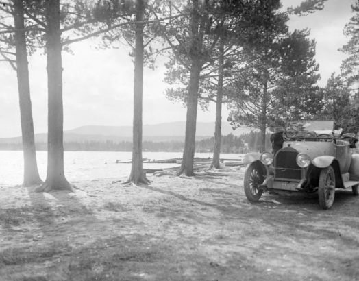 View of a convertible automobile by a lake, among trees, probably in Colorado.