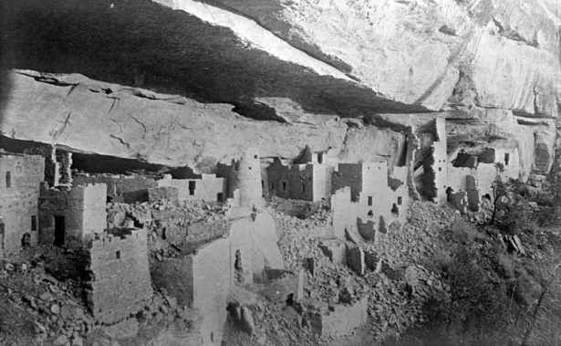 View, facing southeast, of ancient Native American (Anasazi) cliff dwellings before excavation on Chapin Mesa, Mesa Verde National Park, Montezuma County, Colorado. The stone masonry and mud mortar Cliff Palace pueblo homes stand underneath a cliffside overhang. The cylindrical and square ruins have square and T-shaped door openings. Crumbled masonry litters the ground.