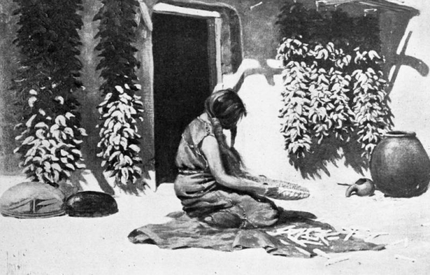 Reproduction of a painting; Native American (Hopi) woman prepares corn on a metate. Behind her is an adobe building, ristras, and pottery.