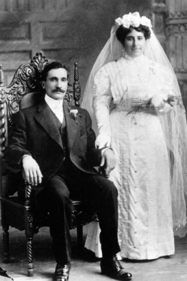 Studio portrait of a husband and wife in the Ricciardi family in Denver, Colorado. The woman wears a wedding dress and veil. The man wears a tuxedo and boutonniere.