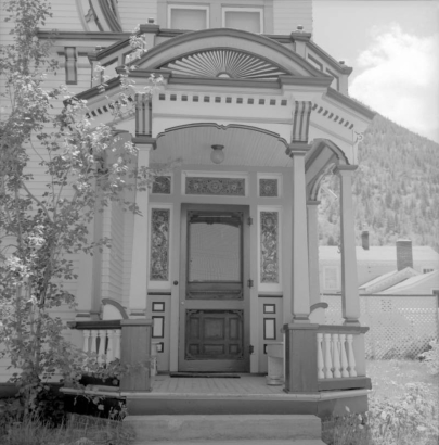 View of the Maxwell House entrance, at at 409 Fourth Street, in Georgetown (Clear Creek County), Colorado. Gothic revival features include columns, capitals, brackets, dentils, a cornice, stained glass, and a pediment with a sunburst pattern.