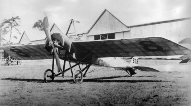 View of a Morane Parasol monoplane by hangars; pilot Georges Guynemer poses.
