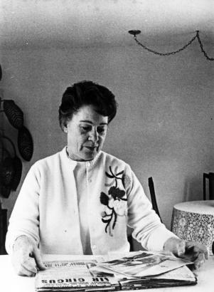 Fay "Rusty" Cox Rogers, parachute jumper, rigger, and instructor, looks through her scrap book. She wears a knit sweater with flower designs.