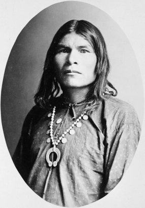Studio portrait of a Native American (Navajo) man. The man wears a shirt and a squash blossom necklace.