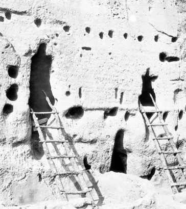 Close-up view of Native American (Anasazi) talus dwellings at Bandelier National Monument, New Mexico. Two ladders rest against irregularly shaped door openings. The tuff dwellings have holes for vigas.