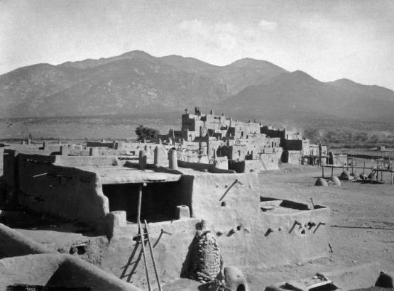 View of north house cluster, Taos Pueblo, New Mexico; shows Native American (Taos) adobe dwellings, ovens, and Pueblo Peak and the Taos Mountains.