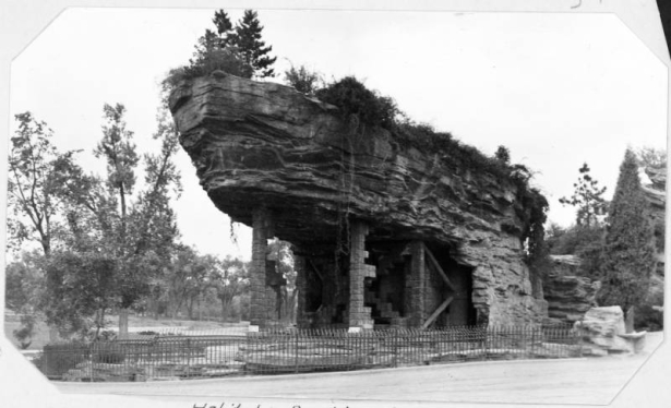 A view of the old bear and sea lion habitat at the Denver Zoo in City Park in Denver, Colorado. Trees and foliage cover the rocks and boulders. The steel and plaster structure was completed in 1918 at the size of 185 feet long and 45 feet high.