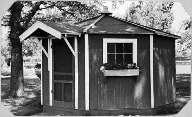 View of the octagonal lawn bowling office in Washington Park, Denver, Colorado. The wood panel building has a window box and covered entrance.