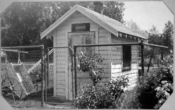 View of a wooden building surrounded by a wire fence at Berkeley Park in Denver, Colorado. A wood cart is supported by the fence. A sign on the building reads: "Danger".