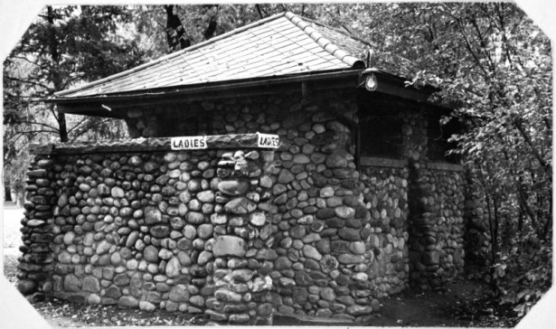 View of the women's restroom at Berkeley Park in Denver, Colorado. The stone building has a tiled roof and a painted sign that reads: "Ladies".
