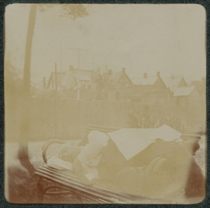 A man sleeps outdoors on a wooden bench in his backyard in Denver, Colorado. Houses are in the distance.