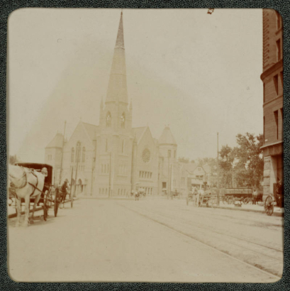 View of Trinity Methodist Church on the corner of 18th (Eighteenth) Street and Broadway in Denver, Colorado. Horse-drawn buggies are in the street. A horse-drawn wagon that reads: "Brown Palace Hotel Citizens Coal Company" is parked near the Brown Palace Hotel.