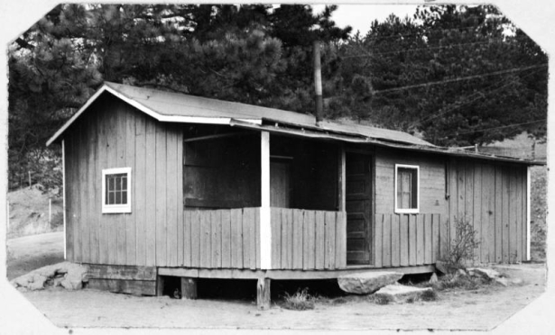 Shows the single story garage and pump house at the Evergreen Golf Course in Dedisse Park 2 miles west of Evergreen, Jefferson County, Colorado. The structure features a small covered porch with a overhang and vertical siding.