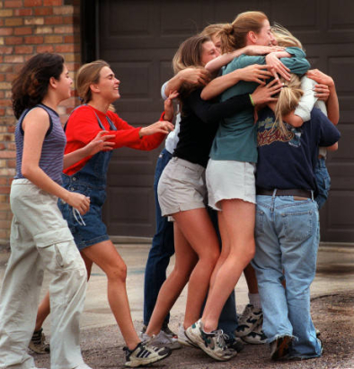 A student just evacuated from the school is embraced by friends overjoyed she is safe.