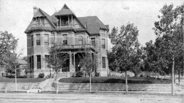 A man, probably Amos Steck, stands on the porch of a house at 1308 Glenarm Place in Denver, Colorado. The three-story brick masonry house has turrets, covered porch, and balconies. Summer, 1886.