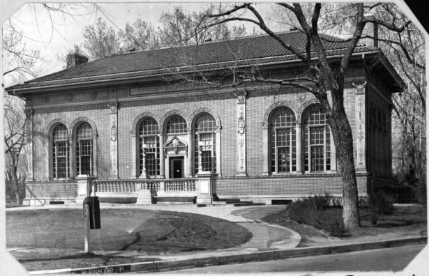 Shows a view of the Roger W. Woodbury branch library in Denver, Colorado located on West Highland Place and Federal Boulevard. The one-story Renaissance style building was designed by J.B. Benedict and features red tiled roof, arched windows and doorways and a front balustrade. The Woodbury Branch was opened in 1913.