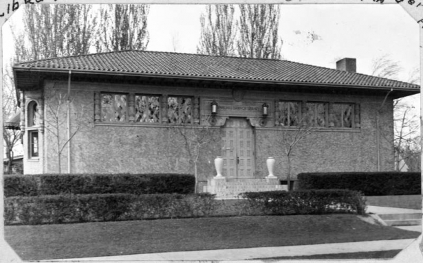 An exterior view of the Park Hill Branch Library located on Dexter and Montview Boulevard in Denver, Colorado. The Park Hill branch library building was built by architects M.R. & Burnham Hoyt and features spanish tiled roof, stucco exterior walls. Two vases are on either side of the brick steps.