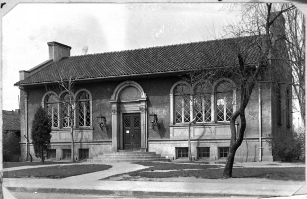 A view of the William N. Byers branch library located on West 7th Avenue and Santa Fe Drive in Denver, Colorado. The one-story building features a stucco exterior, arched windows and doorway, chimneys and red tile roof.