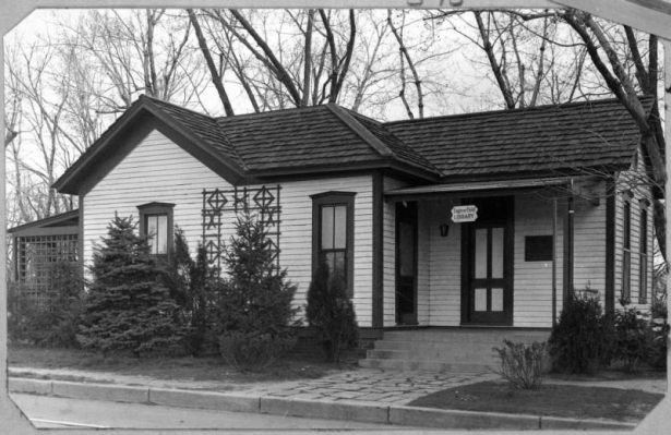 An exterior view of the Eugene Field Library located on East Exposition and South Franklin Street in Denver, Colorado. The single story cottage belonged to Denver poet Eugene Field. The building features wood siding, tiled roof, and a covered porch. A sign that hangs from the porch roof reads: "Eugene Field Library".