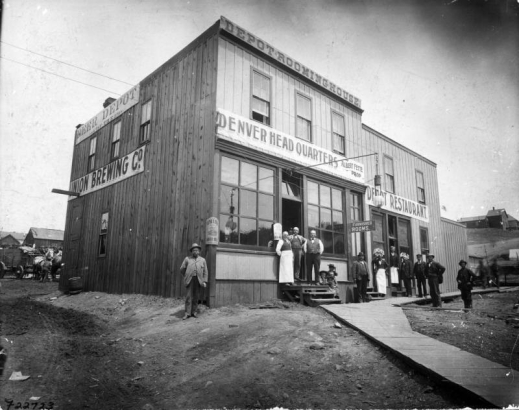 View of businesses at 2433 16th (Sixteenth) Street between Platte and Central (later west Eleventh Avenue) in Denver, Colorado; shows men and girls posing, an electric light, and signs: "Beer Depot Union Brewing Co.," "Depot Rooming House Denver Head Quarters Albert Fette Prop.," "Depot Restaurant."