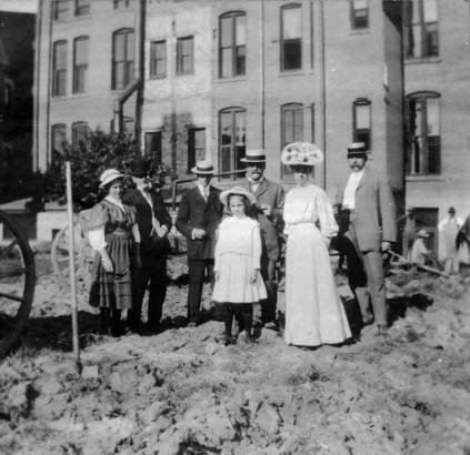 Group portrait of men, women, and girls in Denver, Colorado, at the ground breaking ceremony for the Denver Public Library, including (l to r): Jean Dudley, F. M. Richie, Mr. Frederick Ross (architect), Mr. C. R. Dudley, Helen F. Ingersoll, B. H. Lichter (contractor)[?], and Marion Dudley (in front).