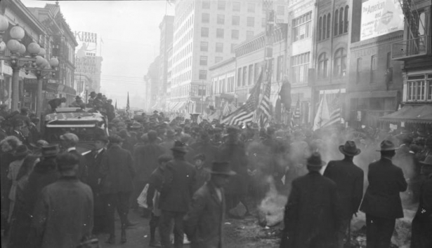 Spectators surround an effigy that hangs from a street light pole to commemorate the end of World War I, on 16th (Sixteenth) Street in Denver, Colorado. A few men hold U. S. flags. Signs read: "Yellow Front", "Bowling", and "Hotel".