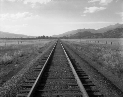 Denver and Rio Grande Railroad tracks pass between fields and hills, in (probably) Colorado.