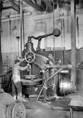 Interior of the Denver Tramway Company machine shop; a worker operates a large drill press.