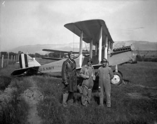 View of men in coveralls (with goggles) and a biplane with letters: "U.S. Navy A-6391," as part of Oil Shale Day in Nada, Garfield County, Colorado.