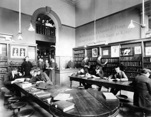 Interior view of the Denver Public Library children's reading room, at the High School, in Denver, Colorado; shows men, women, teenaged boys, shelves of books, sculpture, a balcony / arch, and lettering: "The World is so Full of a Number of Things, I'm sure we should all be as Happy as Kings."