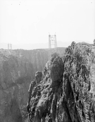View of Royal Gorge Bridge construction in Fremont County, Colorado; shows steel pylons atop granite cliffs, with cable between.