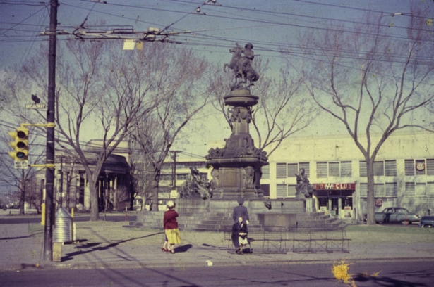 View of the Pioneer Monument at the intersection of Colfax Avenue, Cheyenne Place, and Broadway in Denver, Colorado. A statue on top of the monument depicts a man on horseback. A sign on a building reads: "AAA Auto Club."