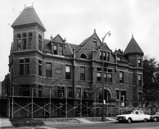 View of the Grace Apartments (under demolition), on Bannock Street in Denver, Colorado; features square and faceted towers, stone arches, finials, and date: "1889." An automobile is parked.