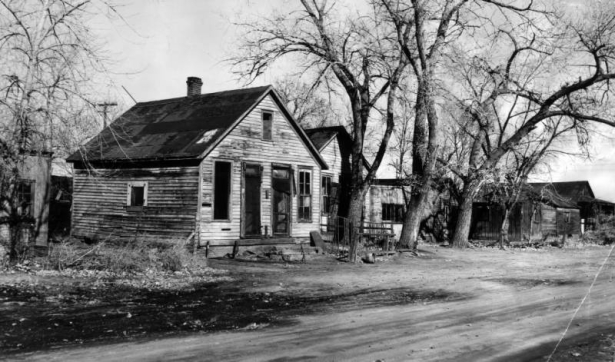 View of abandoned houses on Ninth Street in Denver, Colorado (Lincoln Park Neighborhood); shows dilapidated frame residences and trees.