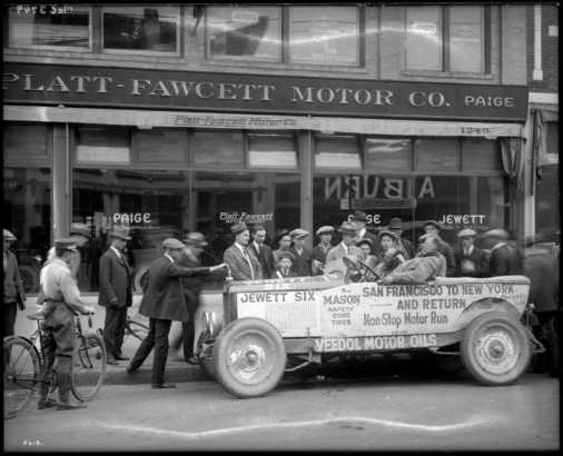 Crowd gathers around automobile crew who just completed an "Automobile Endurance Run" parked in front of the Platt-Fawcett Motor Co., 1249-1255 Broadway, Denver, Colorado; car is a Jewett Six model made by Paige, with lettering on side: "San Francisco to New York and Return, Non- Stop Motor Run, Mason Safety Cord Tires, Veedol Motor Oils;" town names of Reno and Marysville, Calif. are written on car; man with bicycle at left.