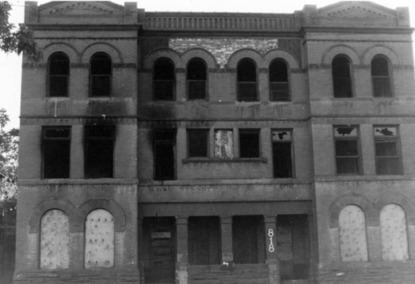 View of an abandoned apartment building at 816 25th Street in the Five Points neighborhood of Denver, Colorado. The three-story building has boarded up arched windows and decorative brick work.