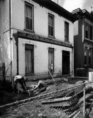 View of 2831 Curtis Street in the Curtis Park neighborhood (Five Points) in Denver, Colorado; shows a brick house with lintels. Men set forms for a new porch foundation.