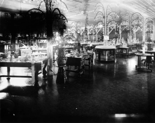Interior view of the Daniels and Fisher store in Denver, Colorado; shows displays of crystal and glass vases and dinnerware; carved wood tables, and a potted palm.