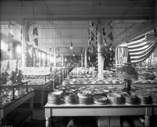 Interior view of the Daniels and Fisher store in Denver, Colorado; shows displays of China dinnerware, cut crystal glass, a lamp, United States and International flags.