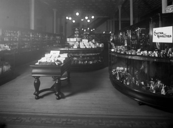 Interior view of the Daniels and Fisher store in Denver, Colorado; shows glass display cases, some with porcelain figurines, a wood parquet floor, and a sign: "Easter Novelties."