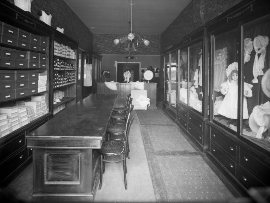 Interior view of the Daniels and Fisher store in Denver, Colorado; shows a counter, chairs, children's shoes, and glass cases with infants apparel and dolls.