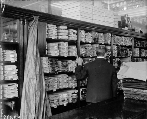 Interior view of the Daniels and Fisher store, in Denver, Colorado; shows bolts of fabric in shelves, and a clerk.