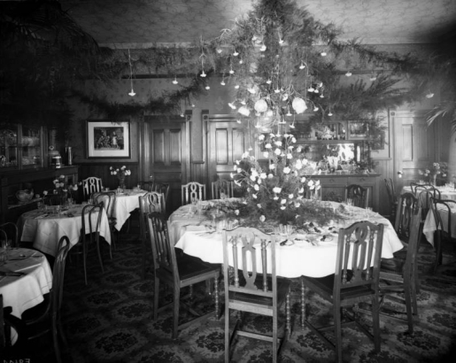 Interior view of a Daniels and Fisher Store showroom, in Denver, Colorado; shows tables set with silver, dinnerware, and arrangements of roses. Garlands hang from lamps.