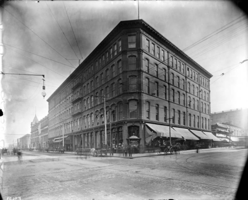 Exterior view of the Daniels and Fisher store in Denver, Colorado; shows storefronts, and horses and buggies.